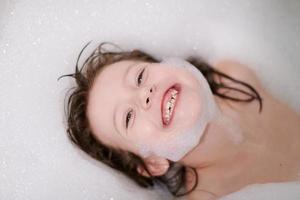 poco ragazza nel bagno giocando con sapone schiuma foto