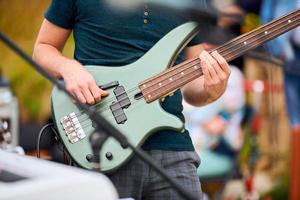basso chitarra giocatore mani, musicista bassista giocando verde basso elettrico chitarra su concerto palcoscenico vivere foto