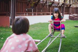 Due ragazza fratelli giocando barcollare vacillare a dondolo con la gioia. asiatico bambino avere dolce Sorridi. bambini rideva brillantemente. 4-6 anno vecchio ragazzo indossare colorato Abiti. giocare nel il terreno di gioco . estate o primavera. foto