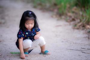 adorabile bambino è raggiungendo per un' piccolo ramo nel il foresta. bambini imparare con natura. ragazza giocare con suolo. prescolastico indossare blu polka punti. contento ragazzo è 3 anni vecchio. foto