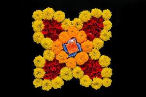 decorativo calendula e rosa fiori rangoli per Diwali Festival con argilla diya lampada illuminato con sfocato messa a fuoco fiamma su nero sfondo. foto