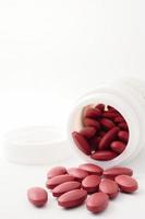 rosso vitamina pillole scrosciante su di il bottiglia su bianca sfondo. foto