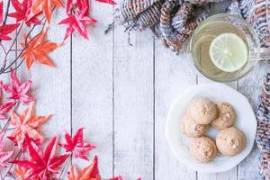 tazza di tè con Limone, biscotto, sciarpa e acero le foglie su bianca dipinto di legno tavolo. foto