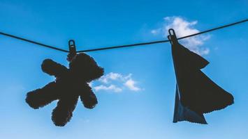 silhouette di orsacchiotto orso e tovagliolo sospeso su il Abiti linea con blu cielo. foto