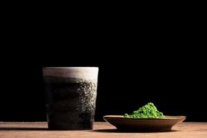 un' ceramica tazza e verde tè polvere su il tavolo, nero sfondo. gratuito spazio per testo foto