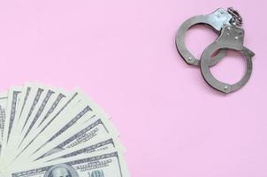 manette della polizia e centinaia di dollari americani giacciono su uno sfondo rosa foto