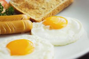 vicino su fritte uova, salsiccia e pane foglio su bianca ceramica piatto. un' popolare cibo di il Hotel e ristorante nel Tailandia. facile per trova e delizioso. foto