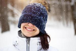 un' donna con un' caldo a maglia cappello tirato al di sopra di sua occhi sorrisi e gode il neve, il primavera sole. all'aperto attività, stagionalità, inverno, neve si scioglie. bianca denti, un' largo, bellissimo Sorridi. avvicinamento foto