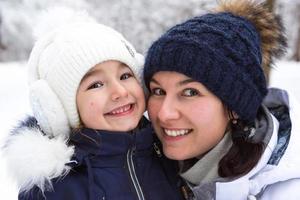 mamma e figlia nel caldo Abiti nel il nevoso foresta abbracciare e guardare in il telaio. inverno divertimento fuori, attivo ricreazione, divertimento nel il freddo . infanzia, forte famiglia. ritratto foto