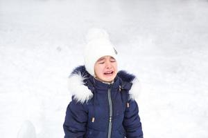 poco ragazza pianto al di fuori nel inverno. un' bambino nel caldo Abiti è rovesciato, freddo, salviette lontano lacrime, urla, è capriccioso e isterico. inverno, neve, brina, figli di isteria, malcontento foto