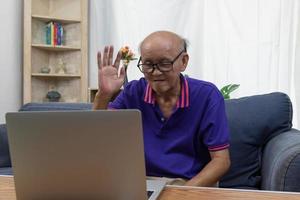 asiatico anziano uomo seduta su il Internet comunicazione video chiamata computer il computer portatile a casa. foto