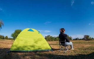 le turiste asiatiche sono sedute felici libere con la tenda verde per il viaggiatore che si siede su un ampio campo, affacciandosi sull'ora serale dell'area privata thailandese per una vacanza in campeggio durante una lunga vacanza per viaggiare. foto