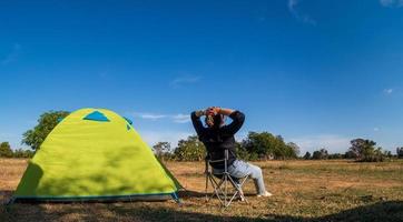 le turiste asiatiche sono sedute felici libere con la tenda verde per il viaggiatore che si siede su un ampio campo, affacciandosi sull'ora serale dell'area privata thailandese per una vacanza in campeggio durante una lunga vacanza per viaggiare. foto