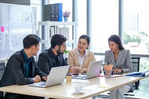 asiatico attività commerciale squadra maschio e femmina colleghi parlando a opera Condividere idee con computer portatile, contento colleghi opera insieme su computer nel ufficio. foto