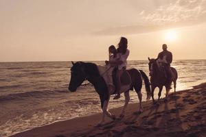 il famiglia spende tempo con loro bambini mentre equitazione cavalli insieme su un' bellissimo sabbioso spiaggia su tramonto. foto