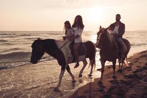 il famiglia spende tempo con loro bambini mentre equitazione cavalli insieme su un' bellissimo sabbioso spiaggia su tramonto. foto