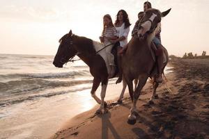 il famiglia spende tempo con loro bambini mentre equitazione cavalli insieme su un' bellissimo sabbioso spiaggia su tramonto. foto