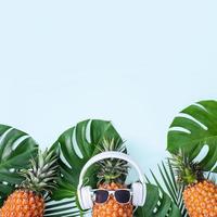 divertente ananas indossare bianca cuffia, concetto di ascoltando musica, isolato su blu sfondo con tropicale palma foglie, superiore Visualizza, piatto posare design. foto