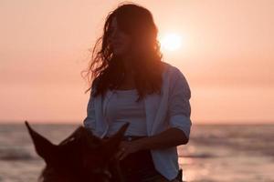 donna nel estate Abiti gode equitazione un' cavallo su un' bellissimo sabbioso spiaggia a tramonto. selettivo messa a fuoco foto