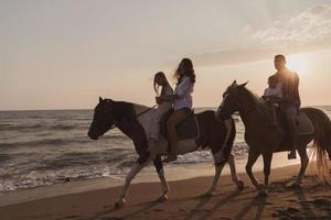 il famiglia spende tempo con loro bambini mentre equitazione cavalli insieme su un' sabbioso spiaggia. selettivo messa a fuoco foto