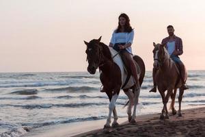 un' amorevole coppia nel estate Abiti equitazione un' cavallo su un' sabbioso spiaggia a tramonto. mare e tramonto nel il sfondo. selettivo messa a fuoco foto