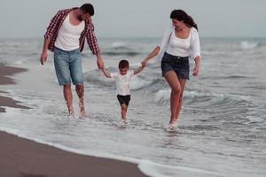 il famiglia gode loro vacanza come essi camminare il sabbioso spiaggia con loro figlio. selettivo messa a fuoco foto