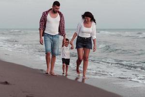 il famiglia gode loro vacanza come essi camminare il sabbioso spiaggia con loro figlio. selettivo messa a fuoco foto