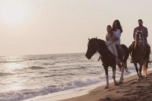 il famiglia spende tempo con loro bambini mentre equitazione cavalli insieme su un' sabbioso spiaggia. selettivo messa a fuoco foto