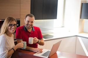 coppia potabile caffè e utilizzando il computer portatile a casa foto