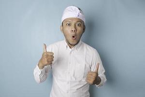 sorpreso balinese uomo indossare udeng o tradizionale fascia per capelli e bianca camicia, isolato di blu sfondo foto