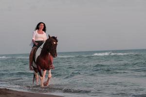 donna nel estate Abiti gode equitazione un' cavallo su un' bellissimo sabbioso spiaggia a tramonto. selettivo messa a fuoco foto