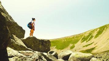 vicino su uno femmina escursionista In piedi su roccia su montagna superiore godere panorama nel caldo estate giorno. ispirazione giovane donna con zaino e escursione nel montagne solo foto