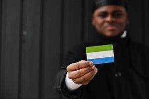 africano uomo indossare nero durag hold sierra Leone bandiera a mano isolato buio sfondo. foto