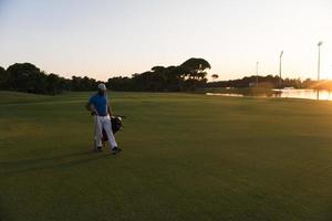 giocatore a piedi e trasporto golf Borsa a bellissimo tramonto foto