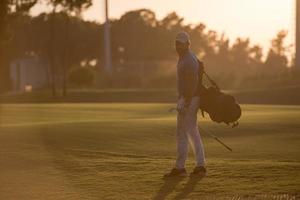 giocatore a piedi e trasporto golf Borsa a bellissimo tramonto foto