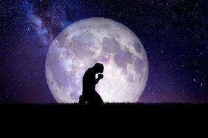 un uomo disperato e solo si inginocchiò e pregò Dio. c'è una luna sullo sfondo di notte. concetti disperati, strazianti e solitari foto