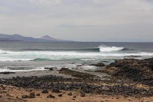 onde dell'oceano turbolente con schiuma bianca battono le pietre costiere foto