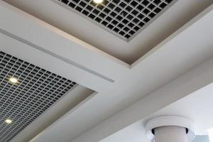 sospeso e griglia soffitto con alogeno macchie lampade e cartongesso costruzione nel vuoto camera nel memorizzare o Casa. allungare soffitto bianca e complesso forma. foto