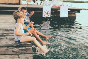 giocoso bambini avendo divertimento mentre seduta su un' molo e spruzzi acqua. foto