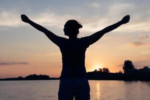 silhouette di spensierato donna con braccia disteso su il spiaggia a tramonto. foto