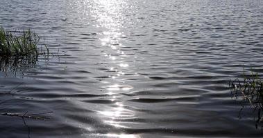bagliore di luce del sole su il superficie di il lago acqua con piccolo onde foto