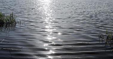 bagliore di luce del sole su il superficie di il lago acqua con piccolo onde foto