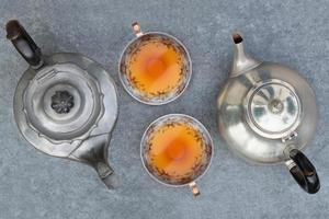 Due diverso vecchio metallo teiere In piedi su un' grigio sfondo. Due identico ceramica tazze da tè siamo pieno con tè e In piedi Il prossimo per ogni Altro. tè per Due fotografato a partire dal sopra. foto
