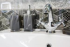 lavandino del rubinetto dell'acqua in ceramica con rubinetto con distributori di sapone e shampoo in costosi bagni o cucine a soppalco foto