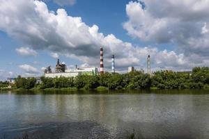 tubi di la lavorazione del legno impresa pianta segheria vicino fiume e ragazzo su kayak. aria inquinamento concetto. industriale paesaggio ambientale inquinamento rifiuto di termico energia pianta foto