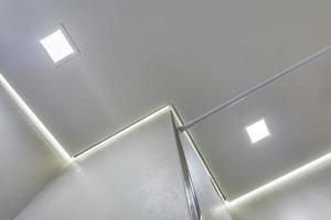 controsoffitto con lampade alogene e costruzione di cartongesso in una stanza vuota in appartamento o casa. soffitto teso bianco e di forma complessa. foto