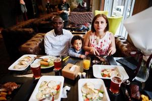 contento multietnico famiglia con ragazzo ragazzo trascorrere tempo a ristorante. relazioni di africano uomo e bianca europeo donna. foto