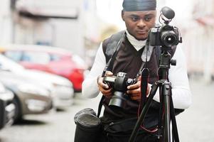 giovane professionale africano americano operatore video Tenere professionale telecamera con tripode professionista attrezzatura. afro cineoperatore indossare nero duraq fabbricazione un' video. foto