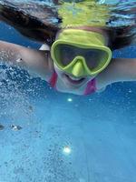 sorridente bambino nel occhiali nuotare, tuffo nel il piscina con divertimento - saltare in profondità giù sott'acqua. salutare stile di vita, persone acqua sport attività su estati. foto