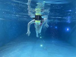 sorridente bambino nel occhiali nuotare, tuffo nel il piscina con divertimento - saltare in profondità giù sott'acqua. salutare stile di vita, persone acqua sport attività su estati. foto